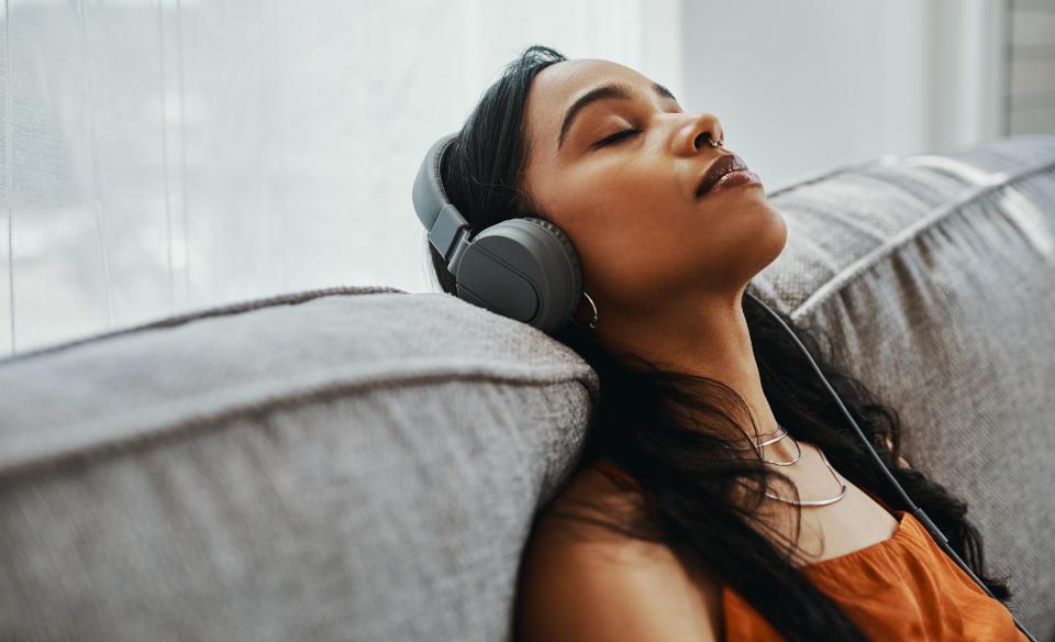 Woman relaxing on sofa with headphones during an online hypnotherapy session